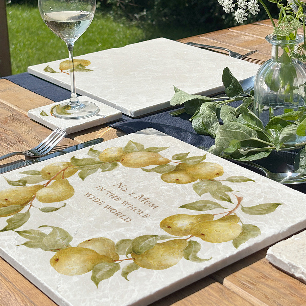 A personalised marble placemat with a pear branches wreath design, with a custom personalised message in the centre. The placemat is on a garden table set for a birthday  dinner.