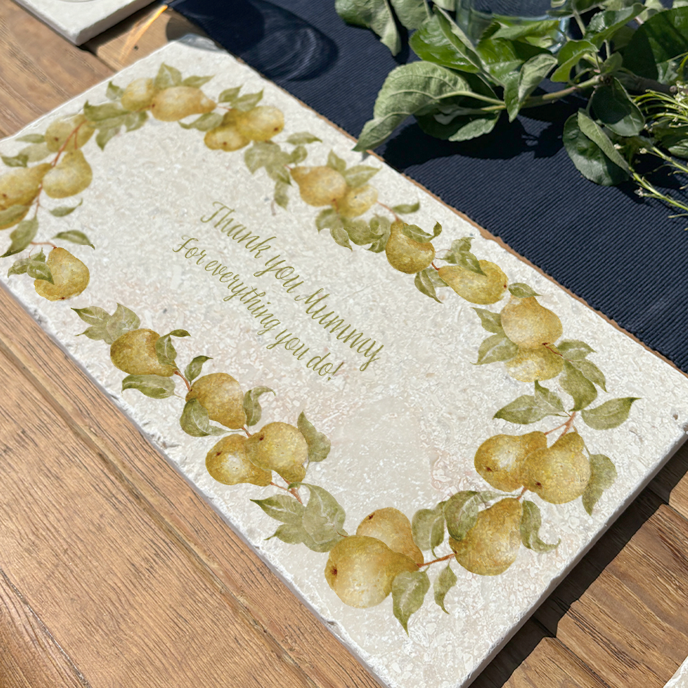 A personalised marble sharing board featuring a wreath of pears and leaves, with a bespoke message in the centre of the design. The custom sharing platter is set on a garden dining table.