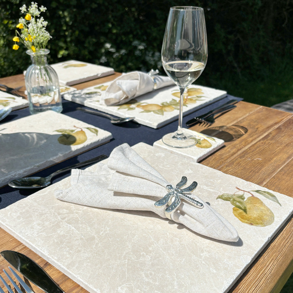 A sophisticated outdoor dining table set with marble placemats and coasters featuring a minimalistic pear design.