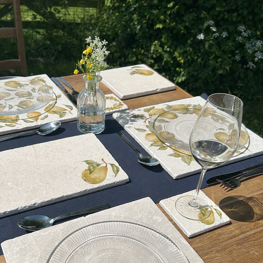 A table laid for an elegant dinner party in the garden, set with marble placemats and coasters that feature a watercolour pear design.