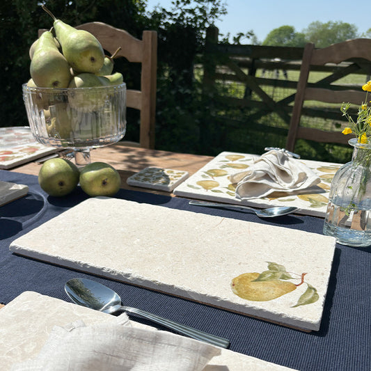 A garden table set with marble placemats and serving platters featuring a minimalistic pear watercolour design.