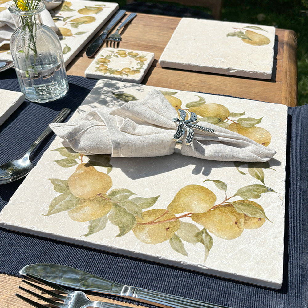 A garden table set for a summer dinner party in the sunshine, the table is set with marble placemats and coasters featuring a rustic pear wreath design.