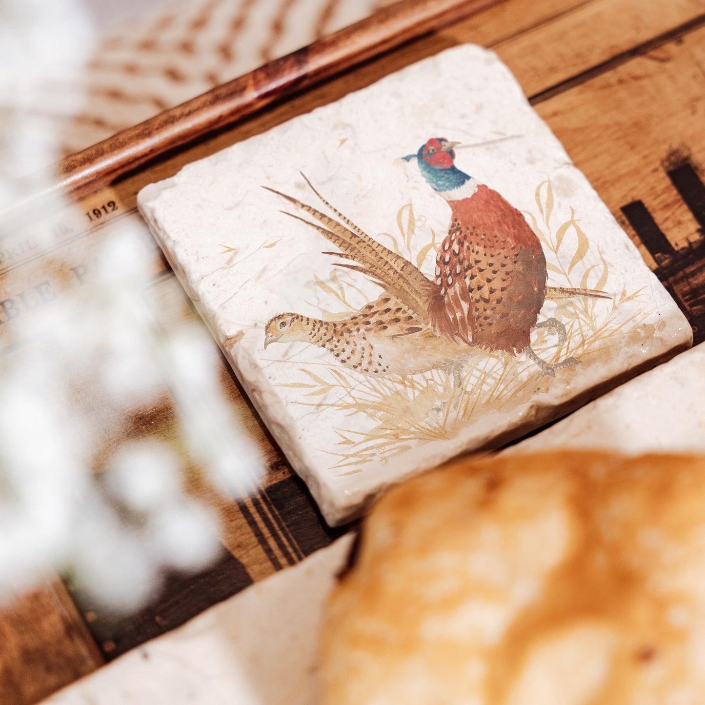 A set of 4 square marble coasters, featuring a watercolour design of a pair of pheasants, one male and one female, in golden grass.