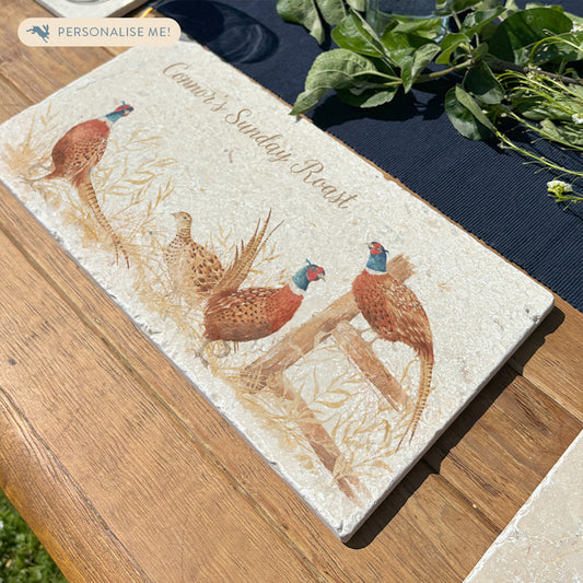 A personalised marble platter with a pheasant design, reading 'Connor's Sunday Roast' in neutral colour text. The platter is set on a dining table ready to be used as a trivet for a roasting dish.