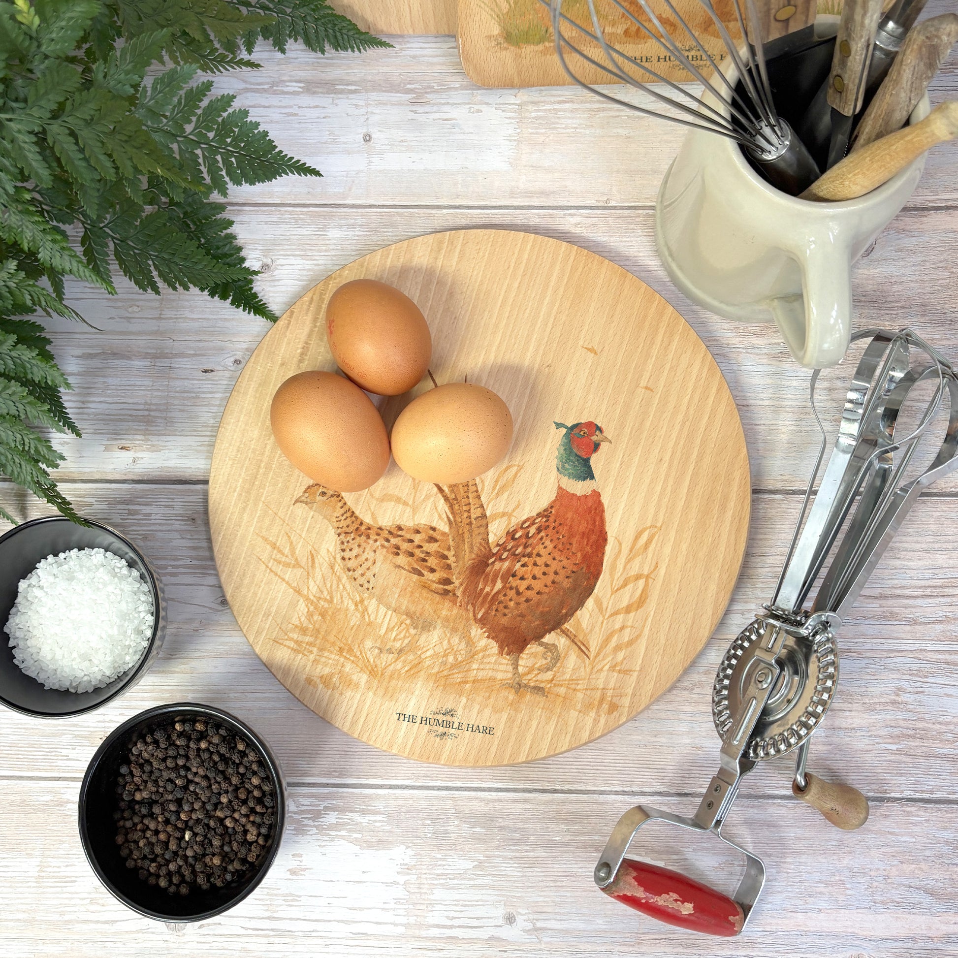 Round wooden chopping board on a kitchen worktop. The beech wood board features a watercolour design of pheasants in the countryside.