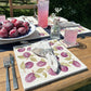 A garden dining table set with marble placemats and coasters featuring a maximalist plum pattern.