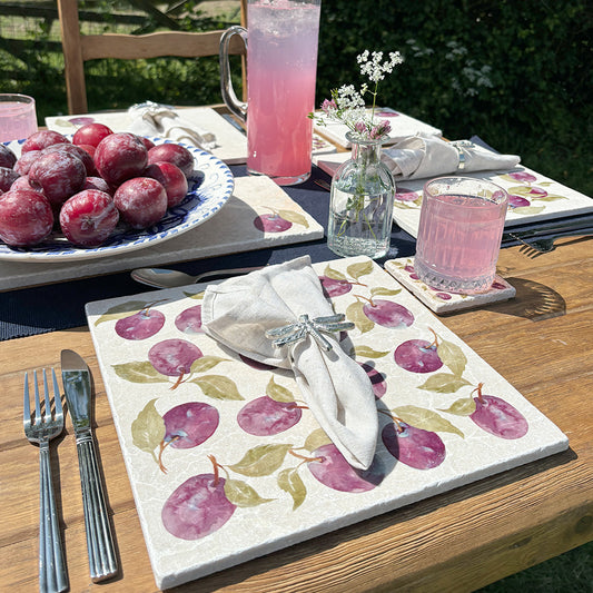 A garden dining table set with marble placemats and coasters featuring a maximalist plum pattern.