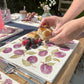 A large marble cheeseboard on an outdoor table with a beautiful pattern of purple plums.