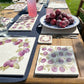 A square medium multipurpose platter used as a side plate on an outdoor dining table. The platter features a maximalist plum pattern.