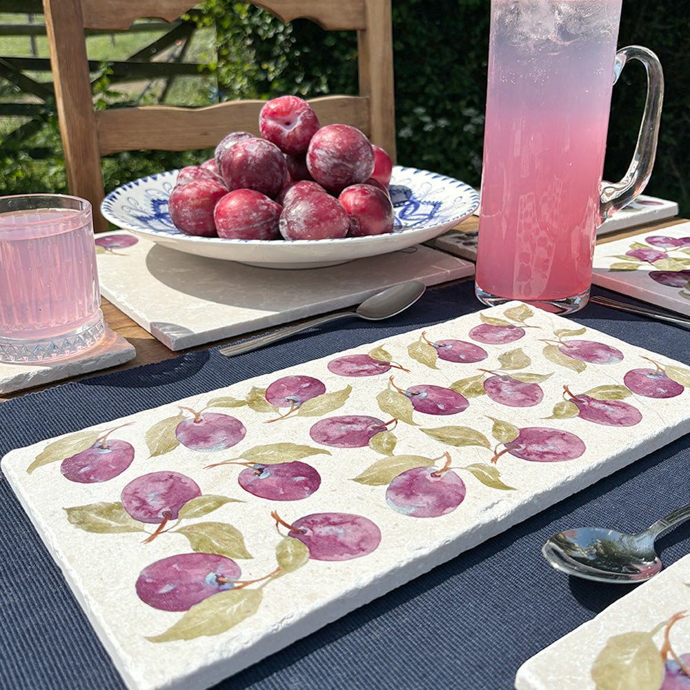 A garden tablescape set with handmade marble platters and coasters ready for a dinner party. The platters feature an elegant purple plum pattern.
