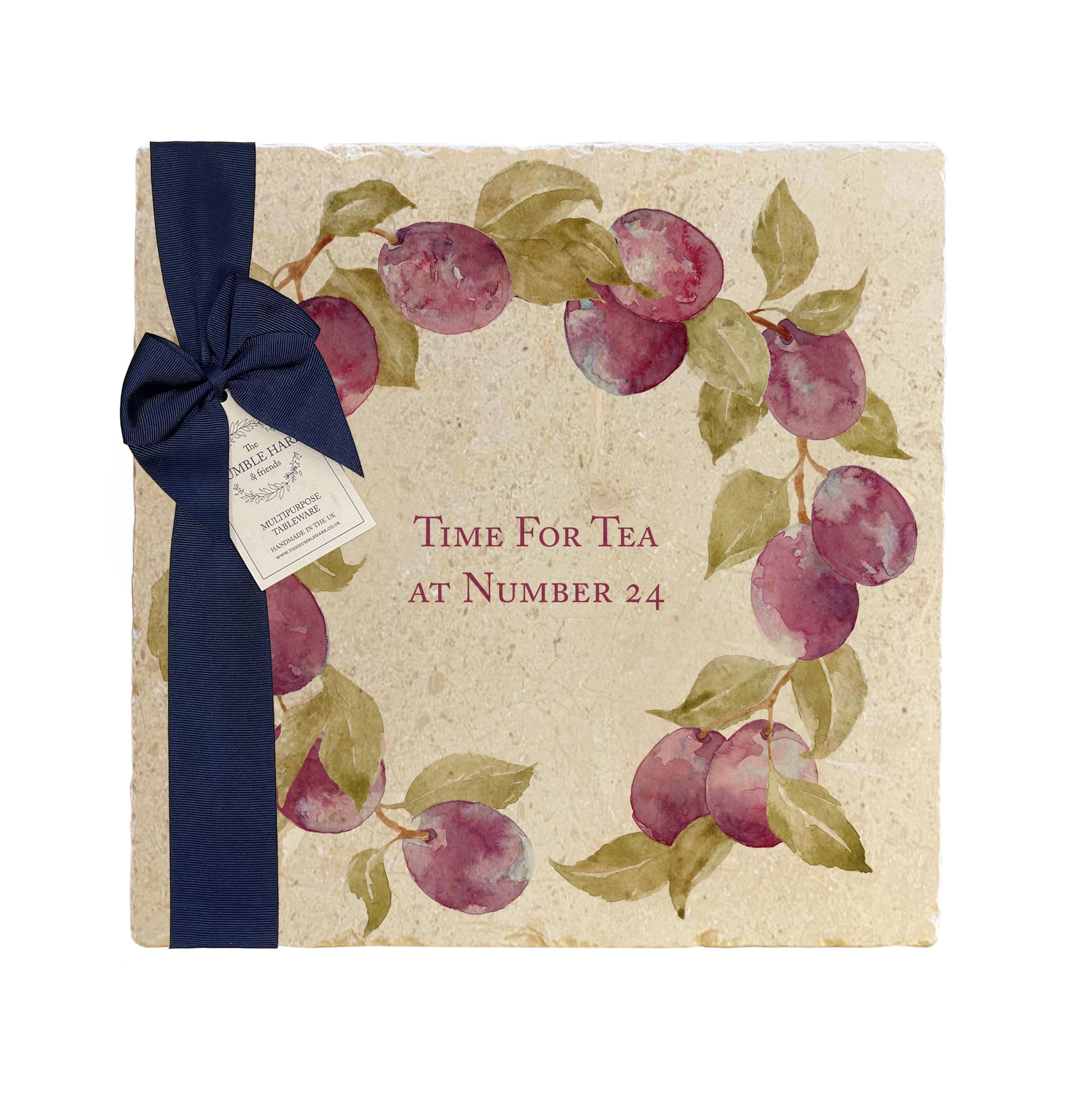 A personalised marble platter featuring a wreath of plums and leaves, with a bespoke message in the centre of the design. The platter is packaged with a luxurious blue gift bow and tag.