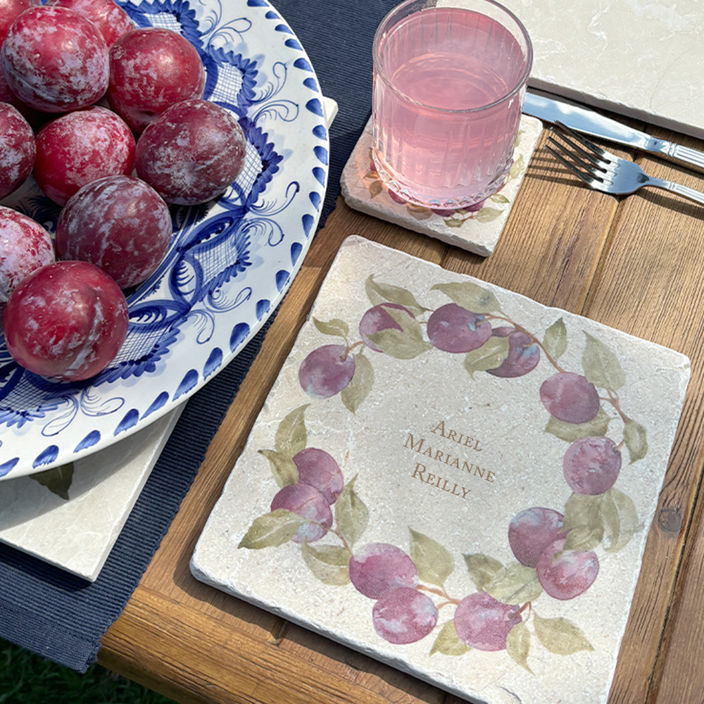 A medium marble serving board personalised with the customer’s choice of names. The serving board is set on a garden table next to a marble placemat in the sunshine.