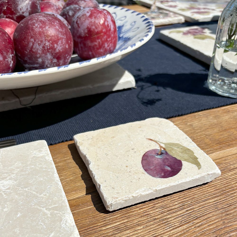 A square marble coaster on a garden table featuring a minimalistic watercolour plum design.