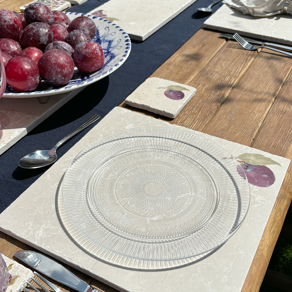 An al fresco dining table set with marble placemats and coasters featuring a minimalistic watercolour plum design.