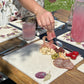 A large marble serving board with a minimalistic plum design, it is being used to serve cured meats, olives, and charcuterie.