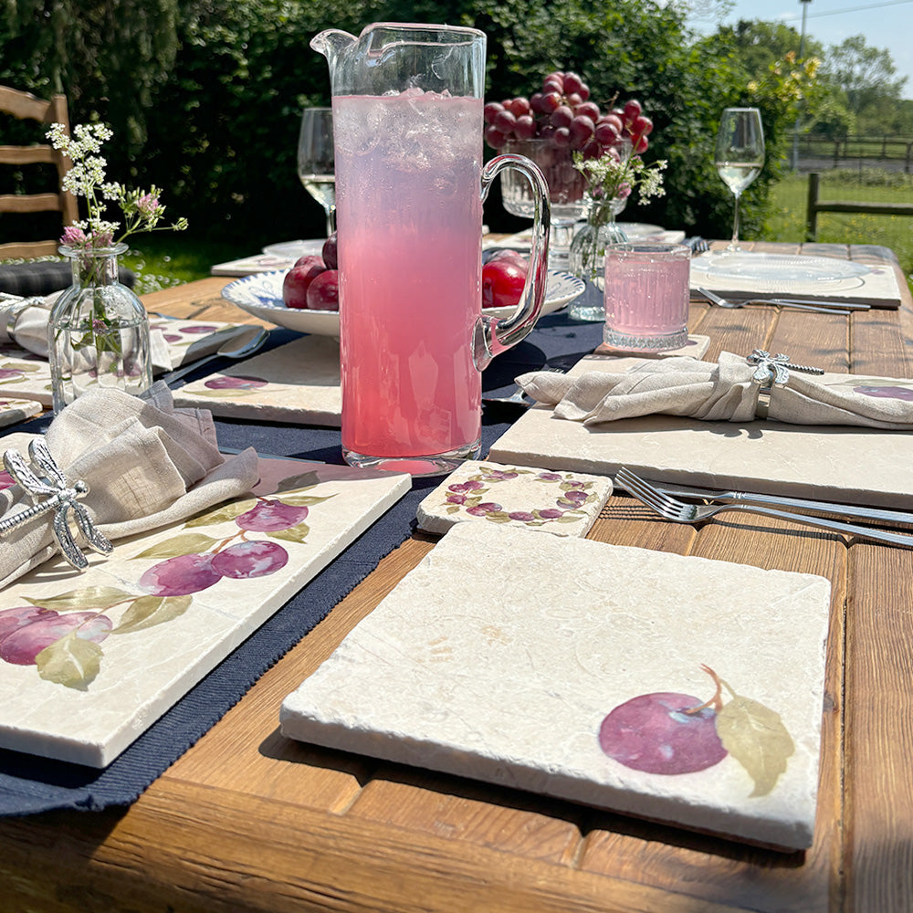 A garden table set with marble placemats and coasters that feature a watercolour plum design.