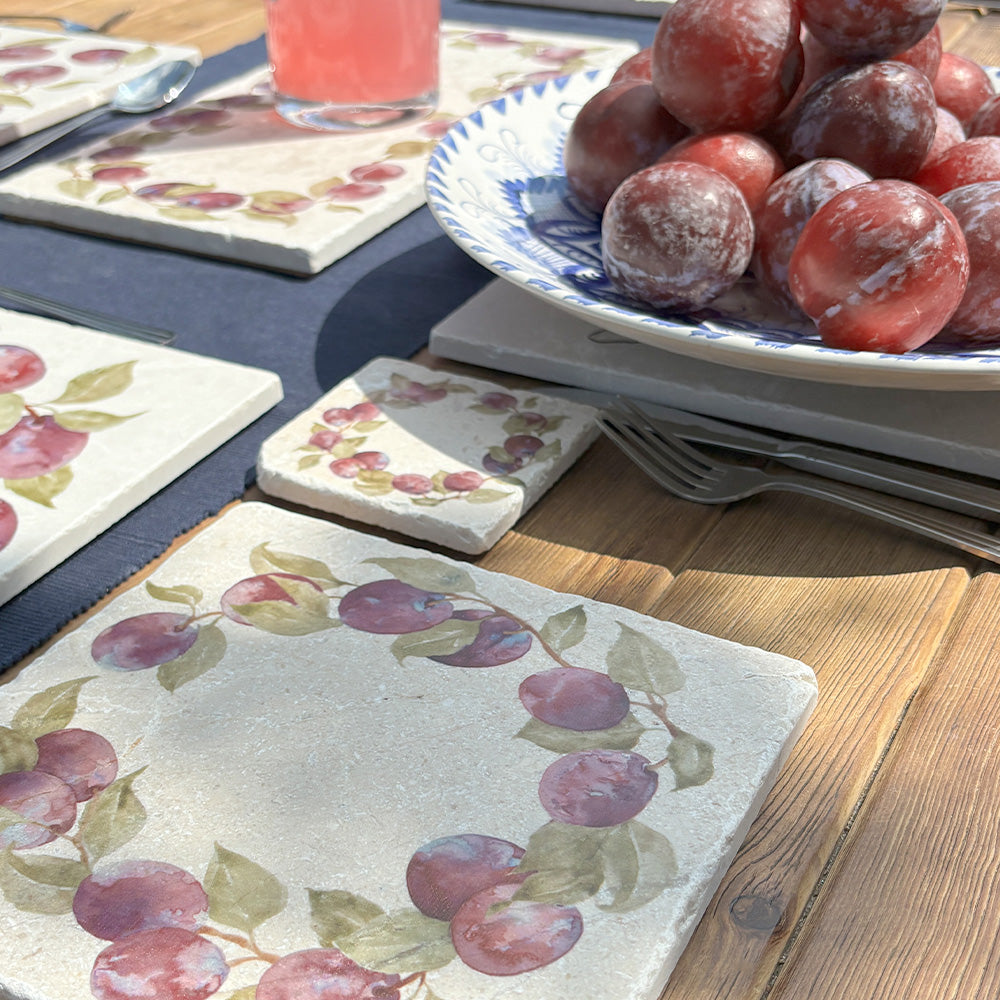 An al fresco dining table set with marble coasters and placemats featuring a watercolour plum wreath design.