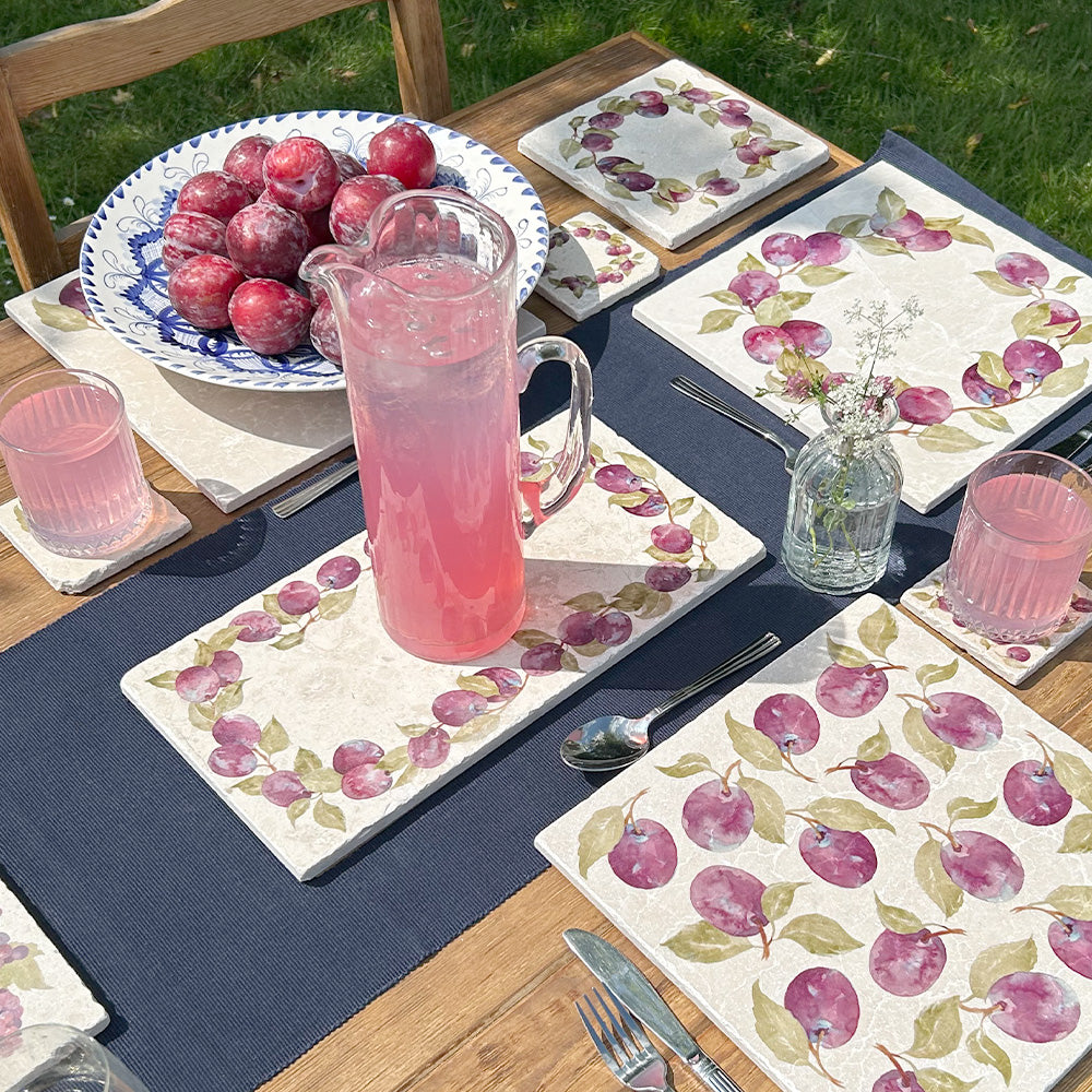 An al fresco dinner table in the garden, set with marble serving platters featuring a vintage plum wreath watercolour design.