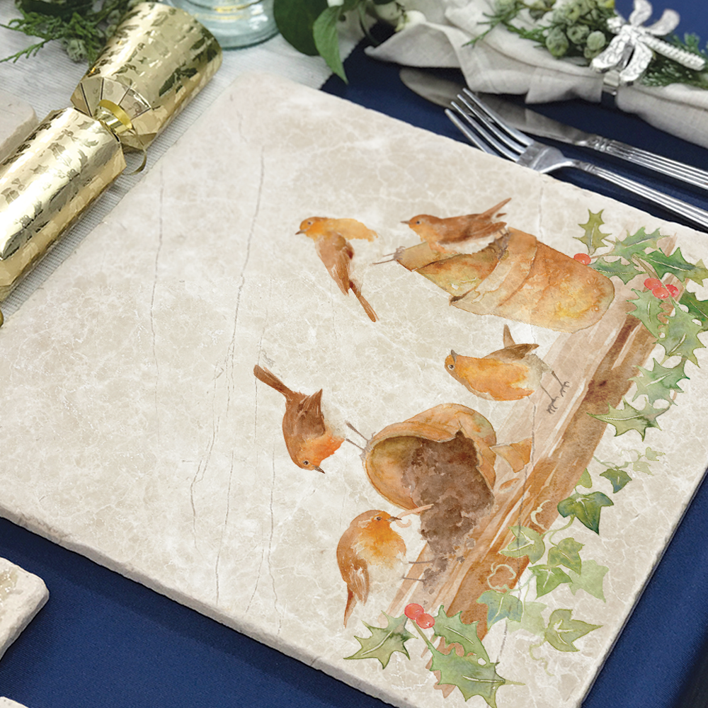 A large marble placemat set on a table laid for Christmas dinner. The placemat features a Christmas robin and holly design.