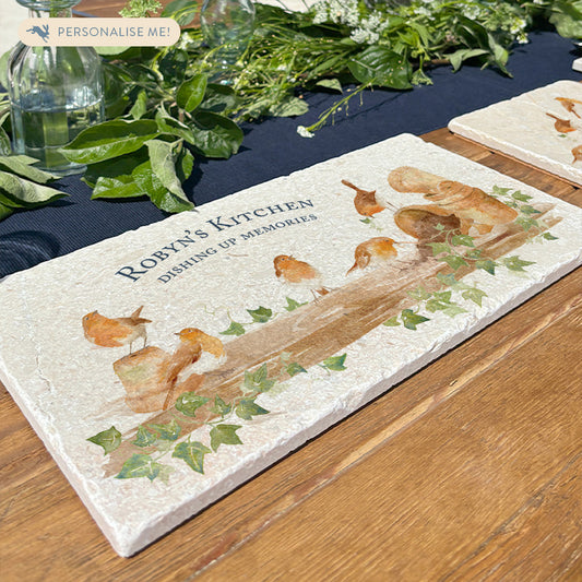 A personalised robin marble sharing platter with dark blue personalised text in a classic serif font. The platter is set on a dining table decorated with fresh leaves and flowers from the garden.