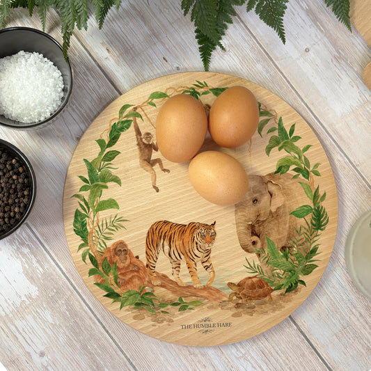 Round wooden chopping board on a kitchen worktop. The beech wood board features a watercolour design of rainforest animals in the jungle.