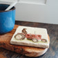 A square marble coaster with a chocolate Labrador retriever dog sat on a vintage red tractor. The coaster is on a kitchen work surface.