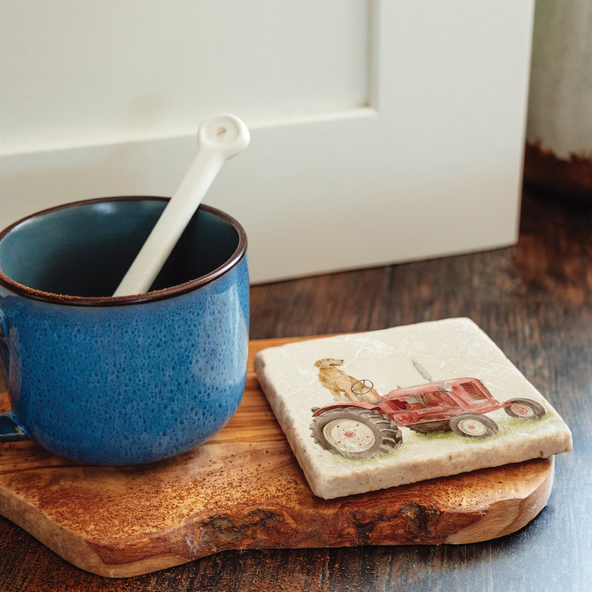 A square marble coaster with a golden retriever dog sat on a vintage red tractor. The coaster is on a kitchen work surface.