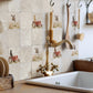 Rustic kitchen backsplash featuring square beige stone tiles with printed red tractor and Labrador retriever dog motifs, installed behind a brass faucet and white sink.