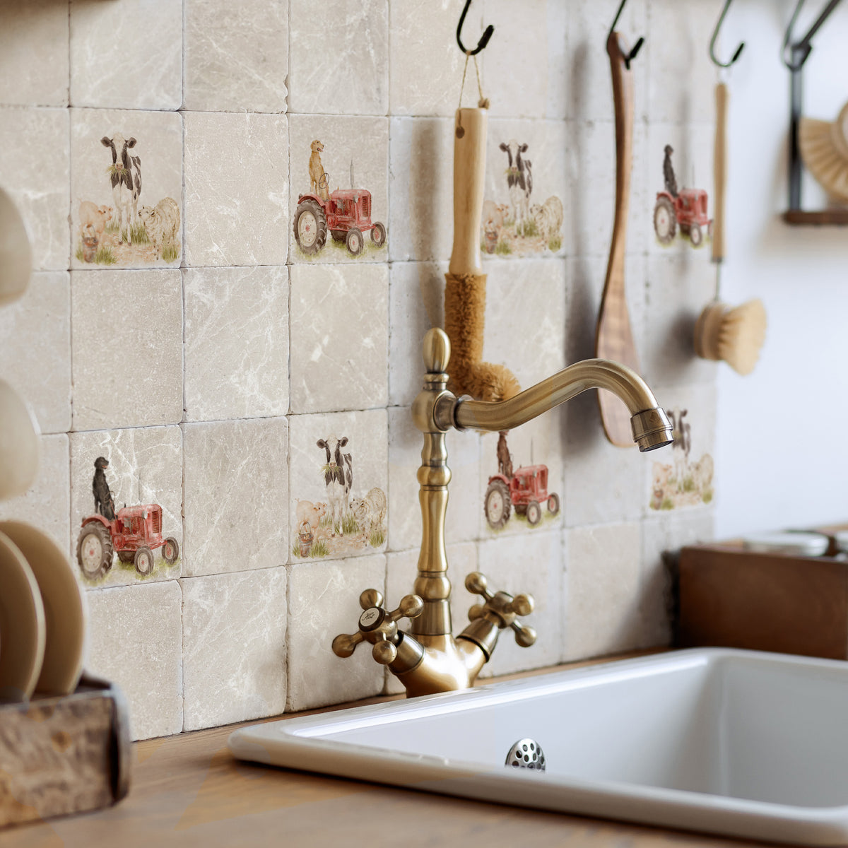 Rustic kitchen backsplash featuring square beige stone tiles with printed red tractor and Labrador retriever dog motifs, installed behind a brass faucet and white sink.
