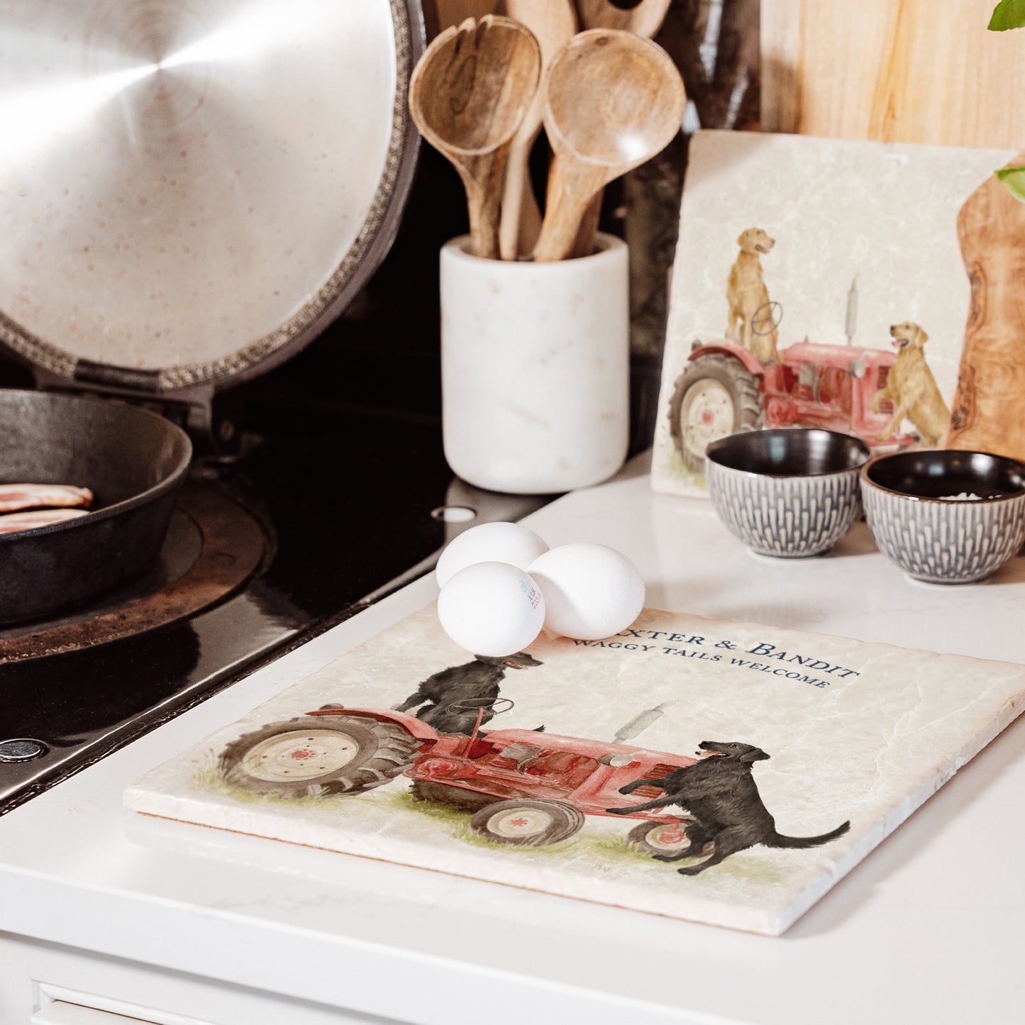 A square large marble platter with black flat-coated retriever dogs sat on a vintage red tractor. The marble platter is sat on a farmhouse kitchen worktop.