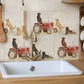A kitchen backsplash featuring beige stone tiles with a pattern of red tractors and Labrador retriever dogs. A white farmhouse-style sink with a brass faucet is installed below the tiled wall.
