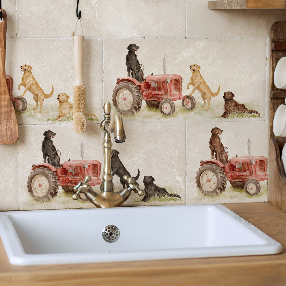A kitchen backsplash featuring beige stone tiles with a pattern of red tractors and Labrador retriever dogs. A white farmhouse-style sink with a brass faucet is installed below the tiled wall.