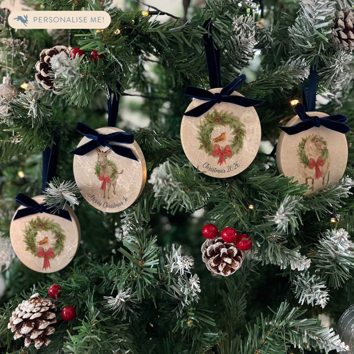 Four oval marble Christmas ornaments hanging on a Christmas tree featuring a robin sitting on a green wreath, with personalised text written below. The ornaments have luxurious velvet ribbon and bow hanging loops.