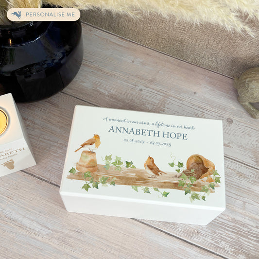Luxury solid wooden white painted Urn with Robins sat on a shelf on pots, a watercolour illustration, our urns and Caskets for displaying or burying ashes. Customisable and can be personalised. Perfect funeral memory keepsake urn, for storing ashes for humans and pets. 