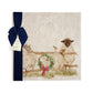 A large square marble platter featuring a watercolour illustration of a farmyard scene of sheep in the snow wearing a Christmas wreath. The platter is packaged with a navy blue bow and paper tag.