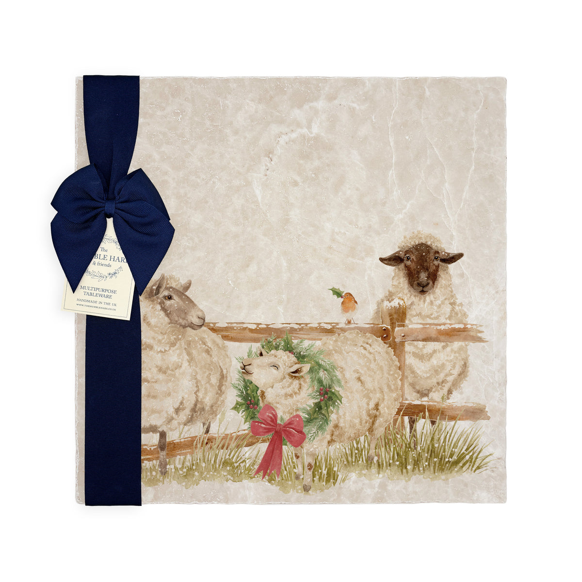 A large square marble platter featuring a watercolour illustration of a farmyard scene of sheep in the snow wearing a Christmas wreath. The platter is packaged with a navy blue bow and paper tag.