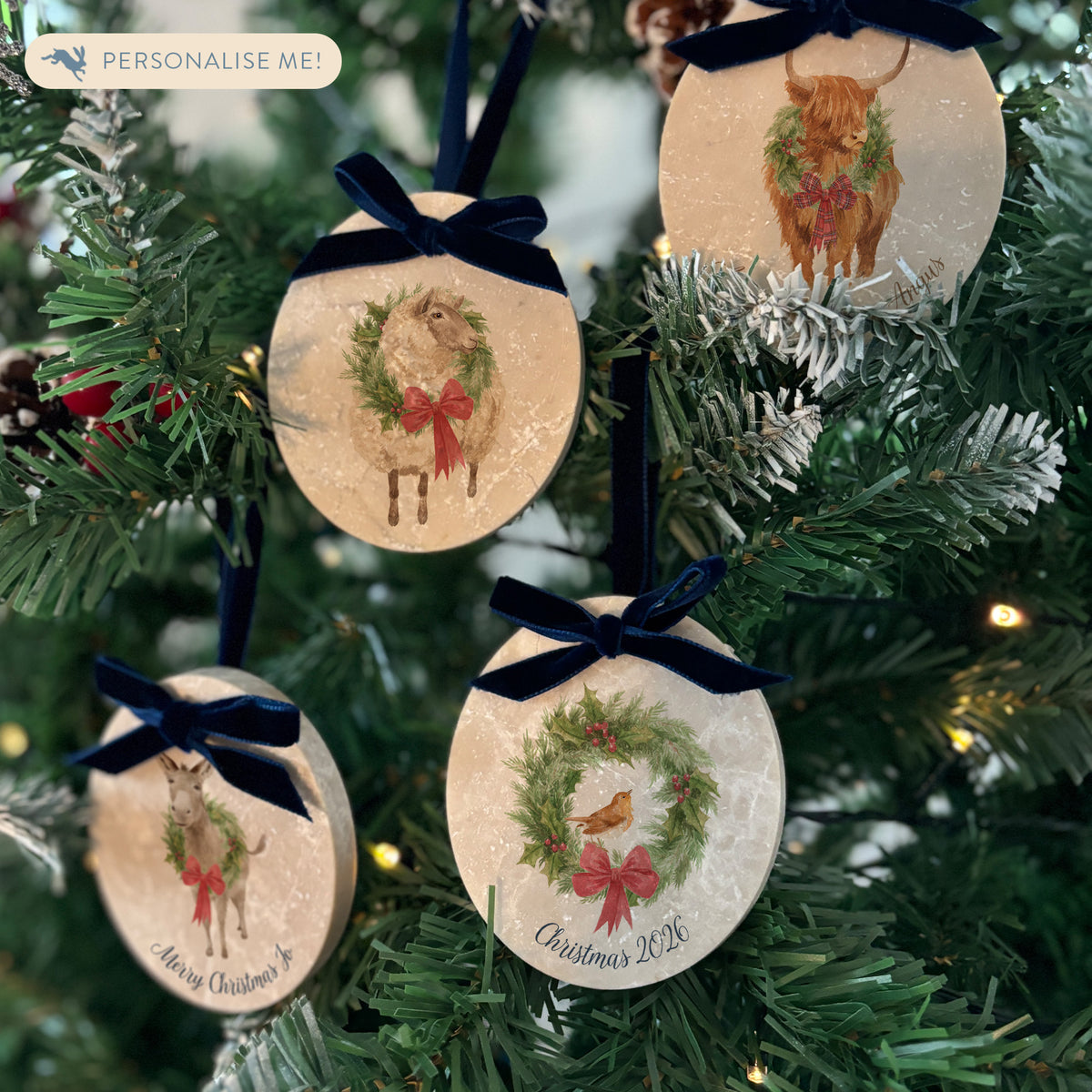 Four oval marble Christmas ornaments hanging on a Christmas tree, featuring a robin, sheep, highland cow, and donkey wearing a green wreath, with personalised text below. The ornaments have velvet ribbons and bows.