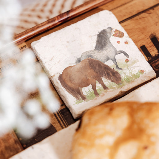 A square marble coaster, featuring a watercolour design of two cheeky Shetland ponies stealing apples.
