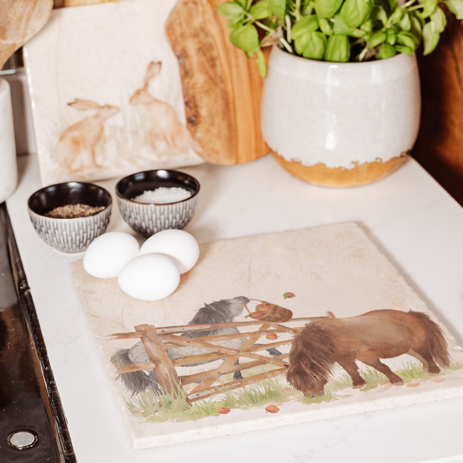 A large square multipurpose marble worktop saver, featuring a watercolour design of two cheeky Shetland ponies stealing apples.