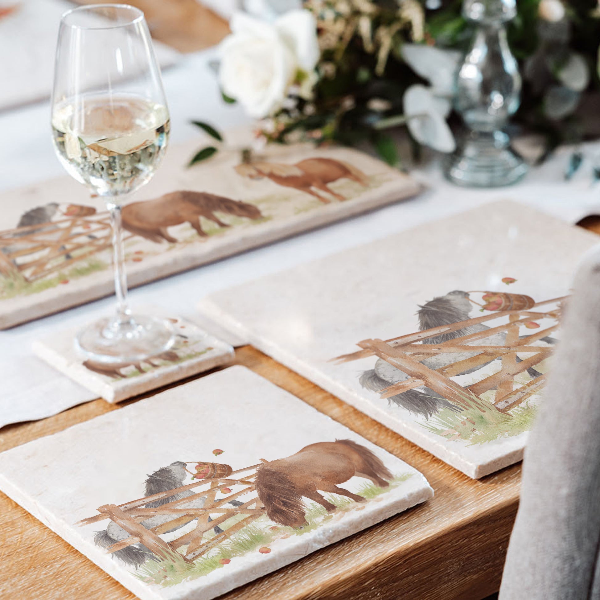 A rustic country table set with marble placemats and platters, all featuring a watercolour design of cheeky Shetland ponies stealing apples.