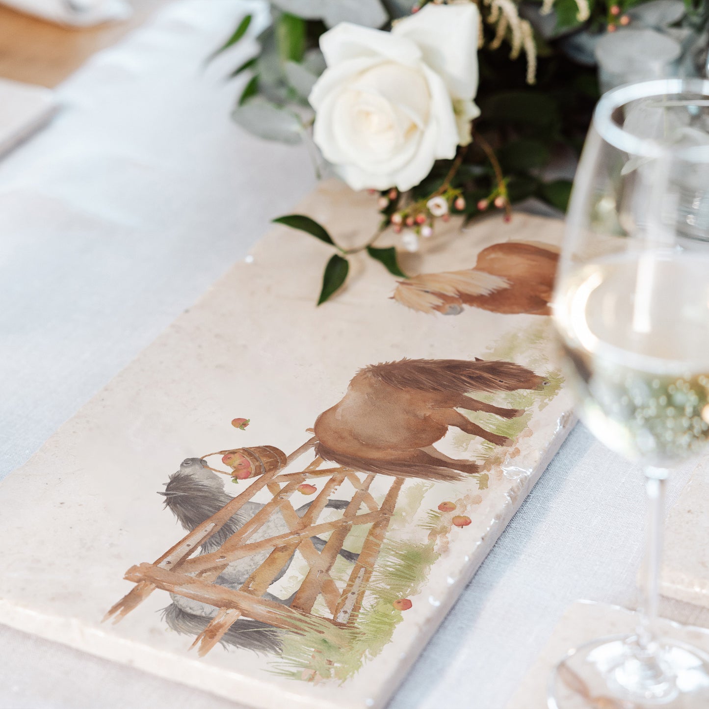 A rustic country dining table set with a multipurpose marble sharing platter featuring a watercolour design of three cheeky Shetland ponies stealing apples.