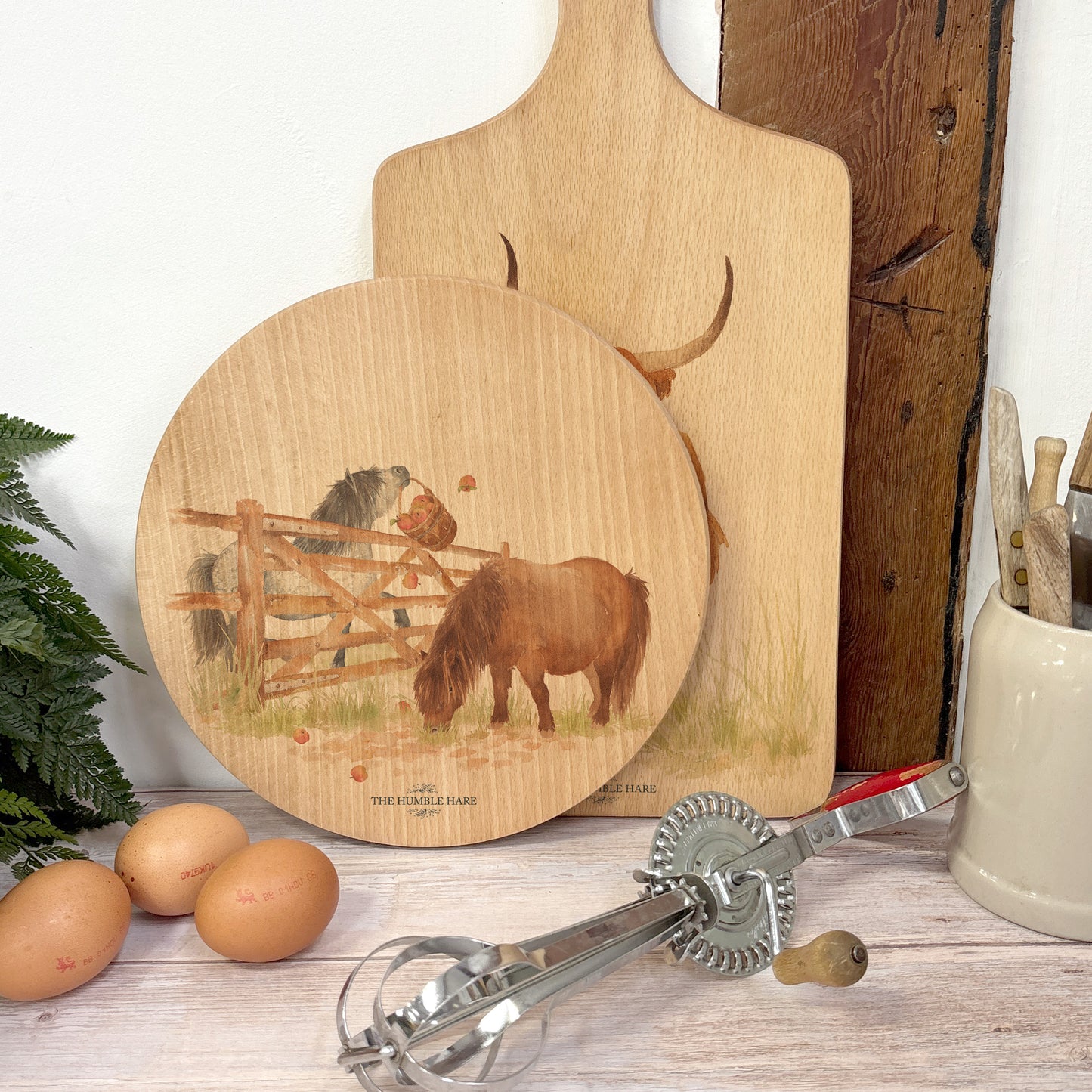 Round wooden chopping board on a kitchen worktop. The beech wood board features a watercolour design of cheeky Shetland ponies.