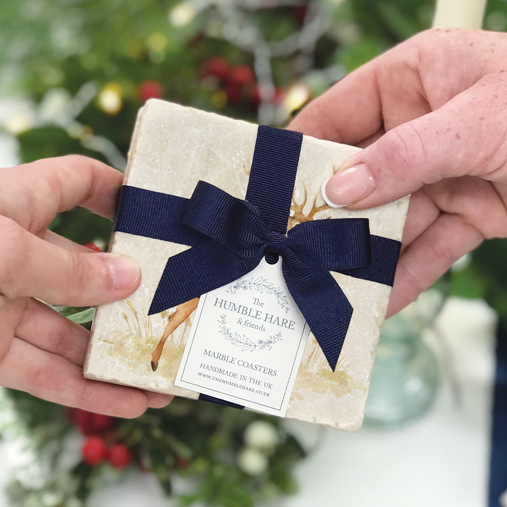 A pair of marble coasters featuring a noble stag design being given as a gift, packaged with a luxurious blue bow and tag.