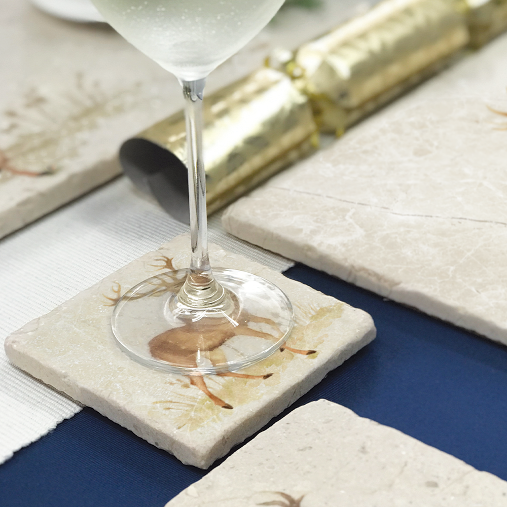 A square marble coaster set on a dinner table. The coaster features a noble stag design in a watercolour style.