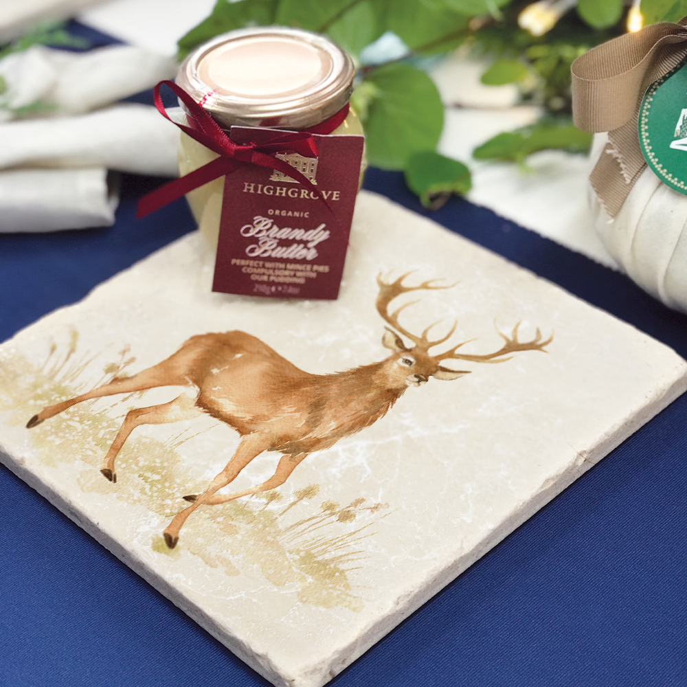 A medium square marble platter featuring a majestic stag in a watercolour style. The platter is set on a table laid for Christmas dinner.