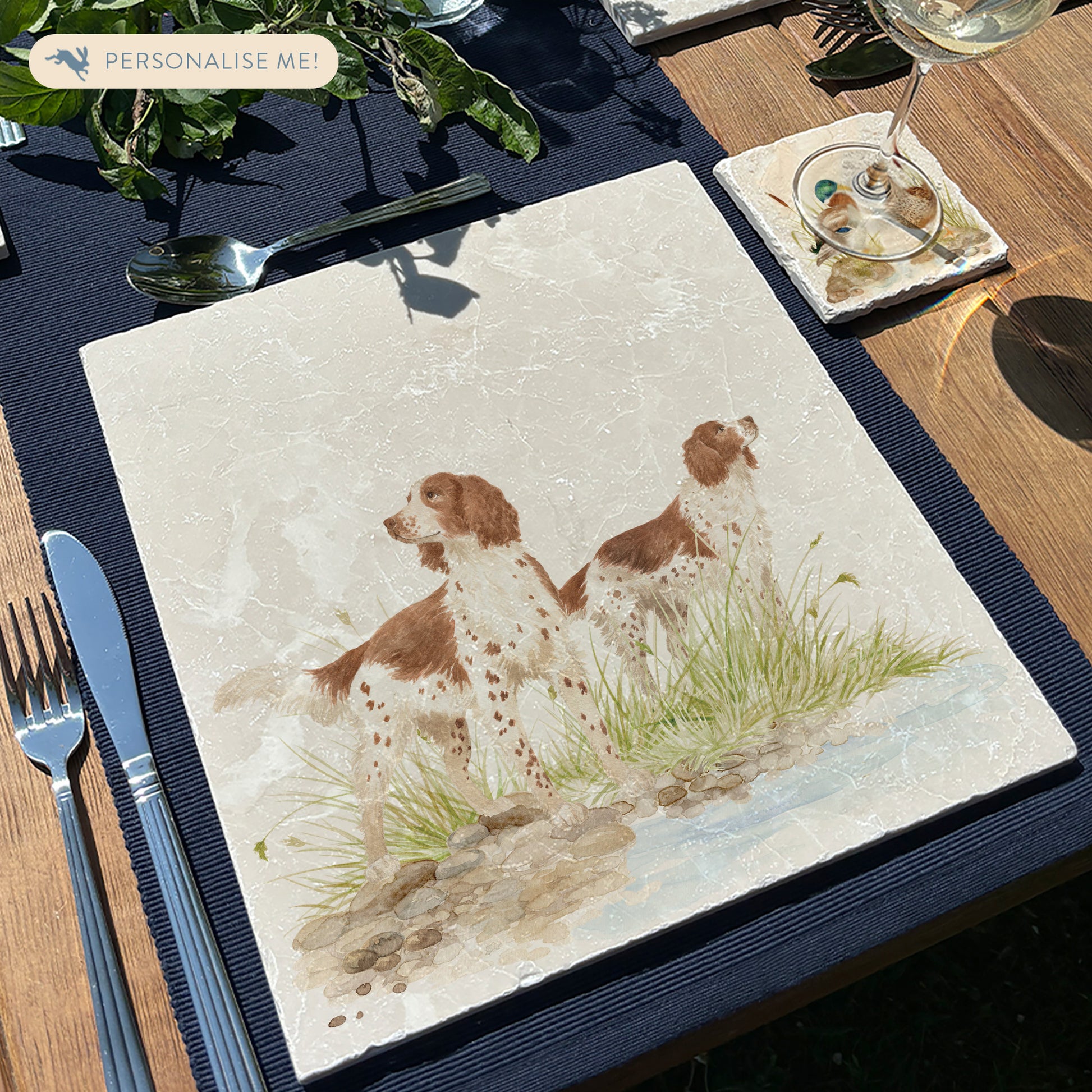 A square large marble placemat featuring a watercolour design of two working spaniel dogs. The platter is set on a wooden table.