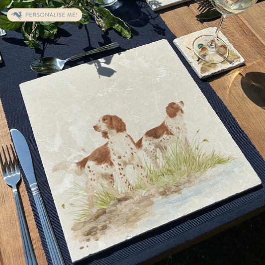 A square large marble placemat featuring a watercolour design of two working spaniel dogs. The platter is set on a wooden table.