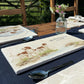 A rectangular marble sharing platter featuring a watercolour design of two working spaniel dogs by a riverbank. The platter is set on a wooden garden table.
