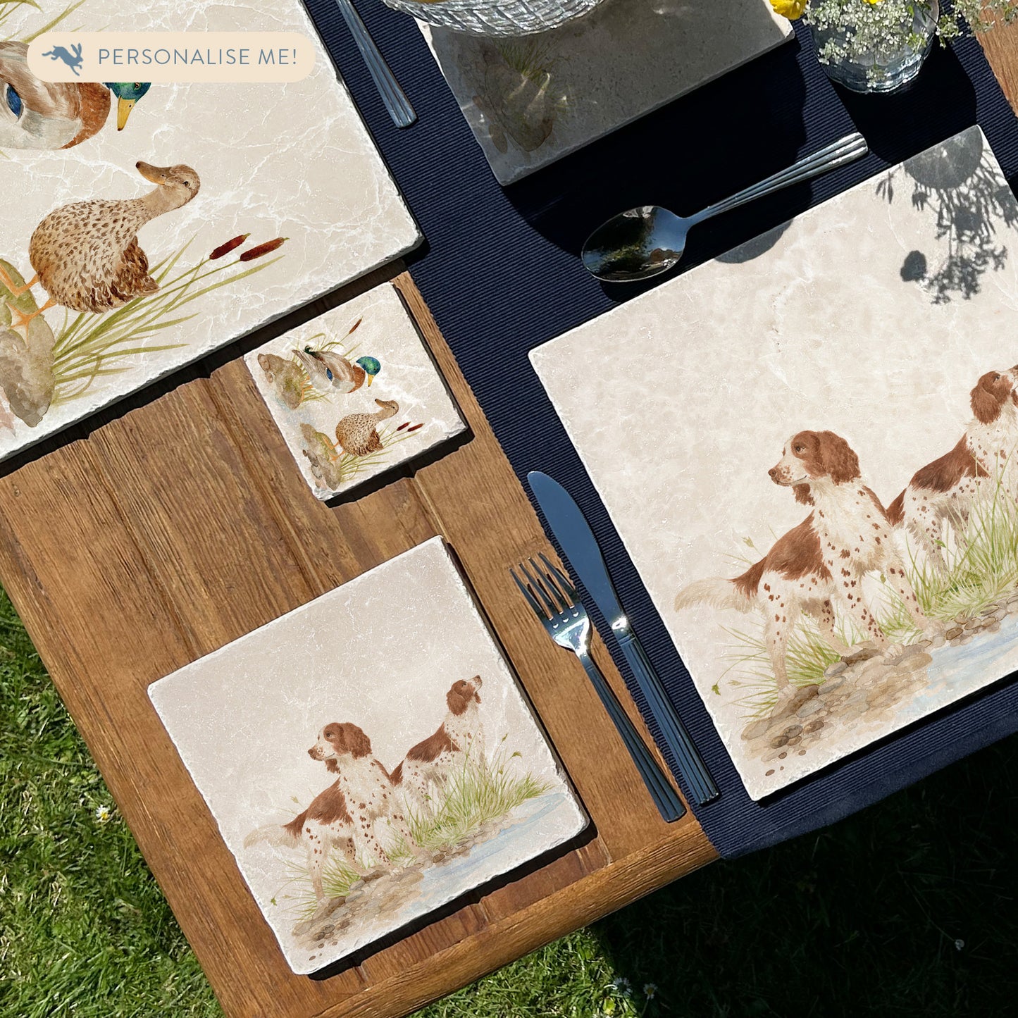 A square medium marble platter featuring a watercolour design of two working spaniel dogs. The platter is set on a wooden table.