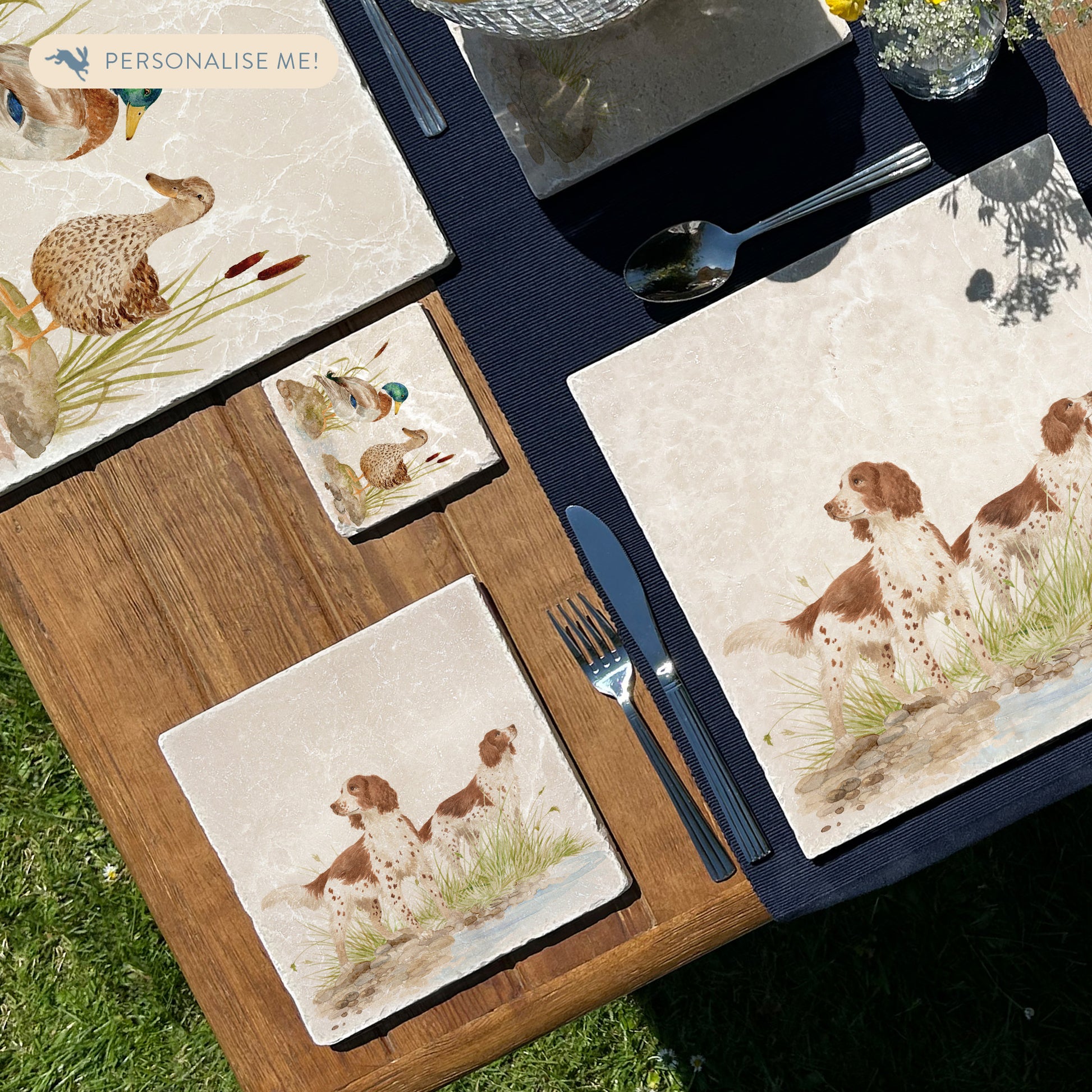 A square medium marble platter featuring a watercolour design of two working spaniel dogs. The platter is set on a wooden table.